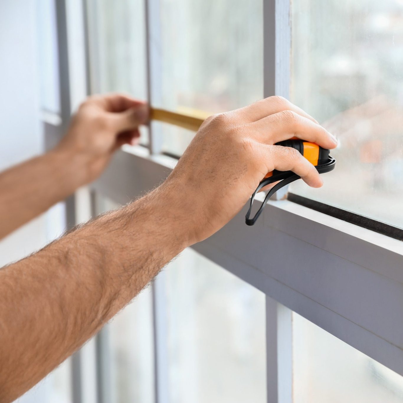 Hände messen einen Fensterrahmen mit einem Maßband.