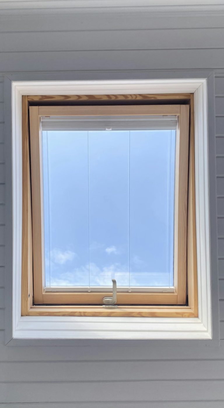Dachfenster mit Holzrahmen und hellblauem Himmel im Hintergrund.