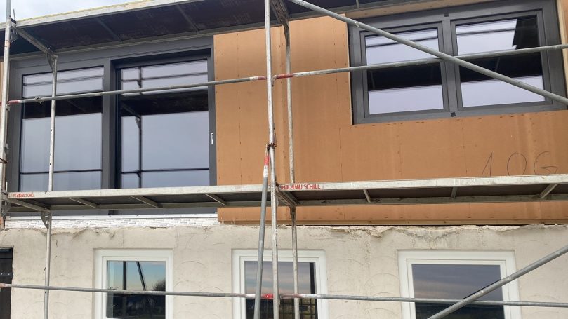 Fassade eines Gebäudes im Bau mit Fenster, Gerüst und unverputztem Bereich.