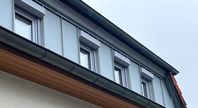 Dachansicht eines Hauses mit mehreren Fenstern und grauer Fassade.