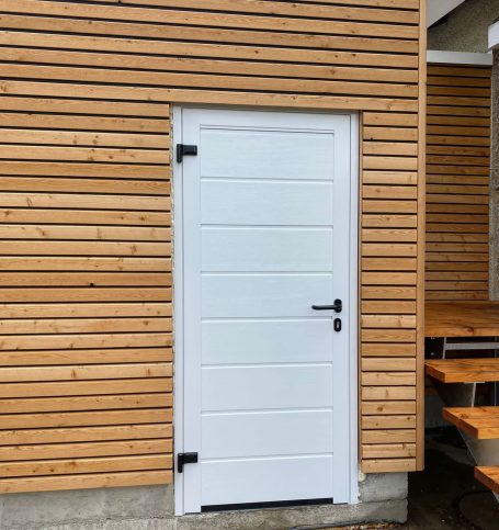Weiße Tür mit zwei schwarzen Beschlägen an einer Holzfassade.