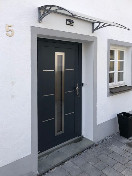 Moderne Haustür in dunkler Farbe mit eleganten Metallakzenten und breitem Fenster.