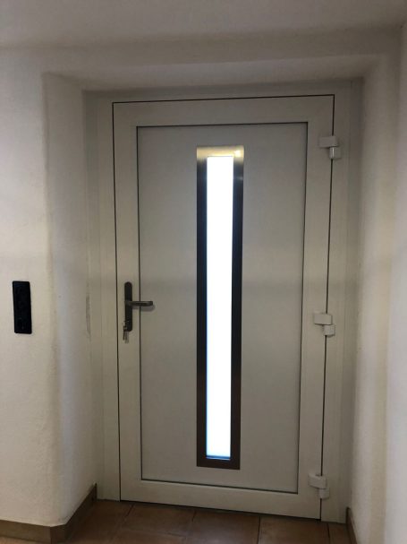 Weiße Tür mit schmalem vertikalem Fenster und schwarzem Türgriff.