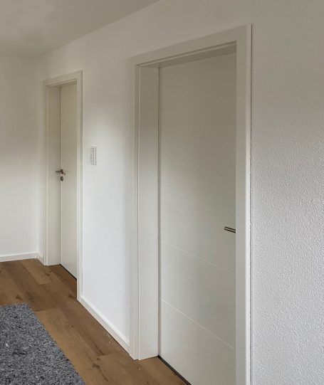 Zwei weiße Türen in einem neutralen Raum mit Holzboden.