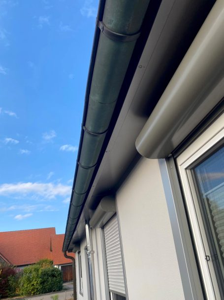 Dachtraufe mit Regenrinne und klarem blauen Himmel im Hintergrund.