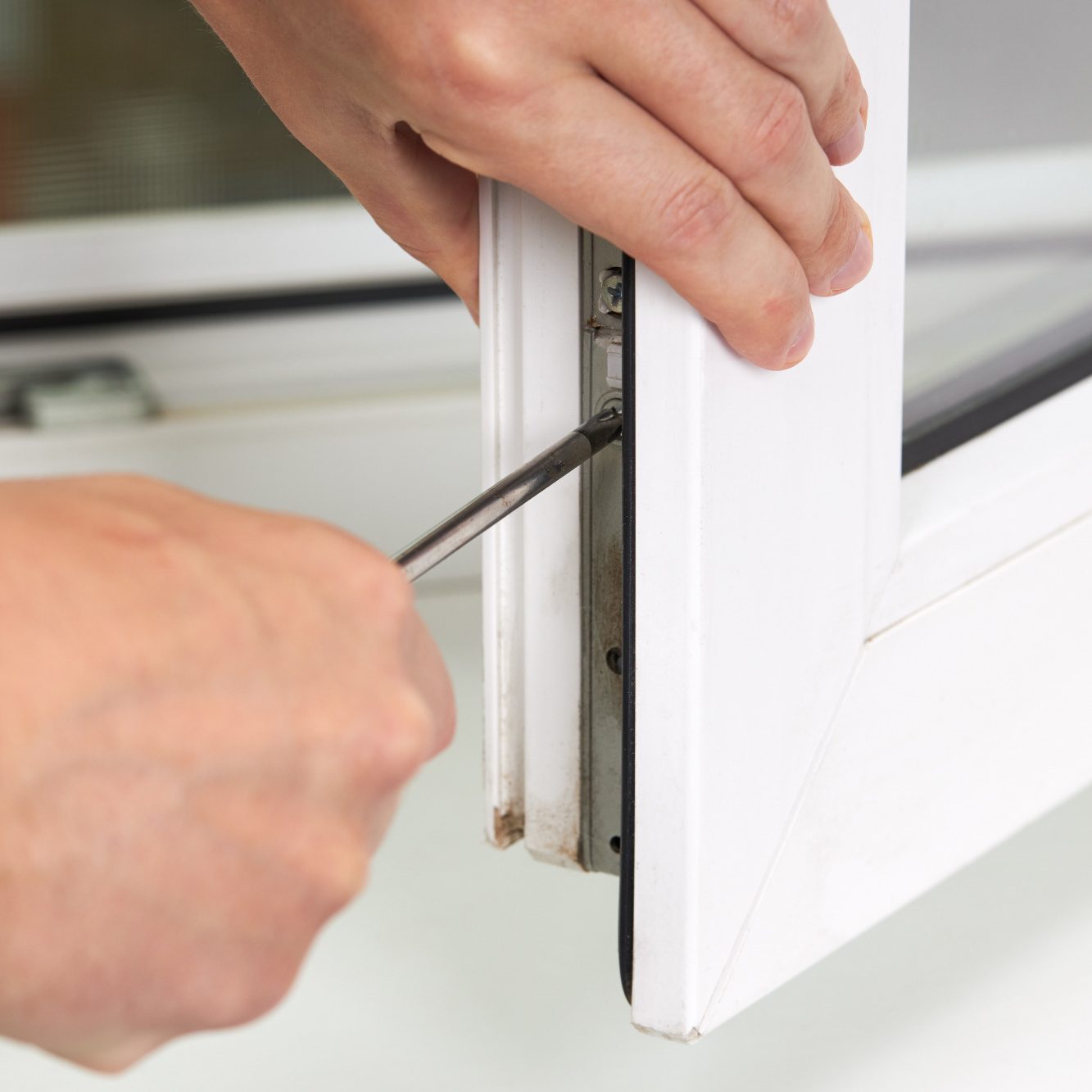 Eine Hand, die mit einem Schraubendreher an einem Fensterrahmen arbeitet.