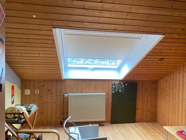 Räumlicher Dachboden mit Holzverkleidung, Dachfenster und Heizkörper.