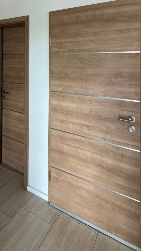 Zwei holzfarbene Türen mit horizontalen Linien in einem hellen Raum.