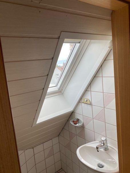 Dachgeschossbad mit schrägem Fenster, Waschbecken und Fliesen.